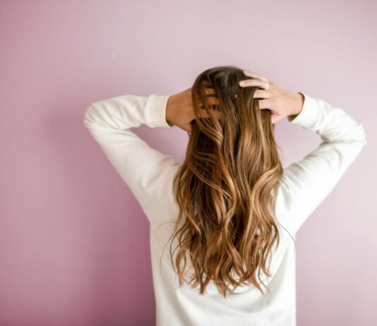 건강한 모발을 위한 생활 습관과 관리법 woman in white long-sleeved shirt standing in front of pink wall