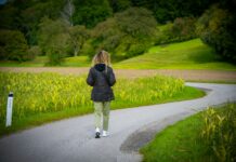 일상 속 ‘마음 챙김 걷기’, 스트레스 관리와 건강 두 마리 토끼 잡는다 Woman walking on a winding road through fields.