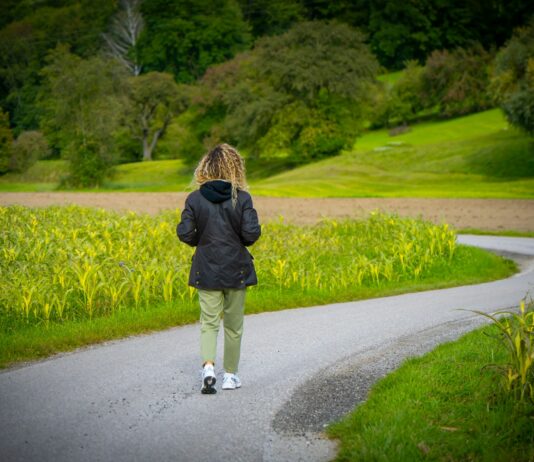 일상 속 ‘마음 챙김 걷기’, 스트레스 관리와 건강 두 마리 토끼 잡는다 Woman walking on a winding road through fields.